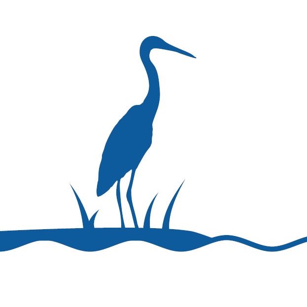 Blue silhouette of a heron standing in shallow water among grass.