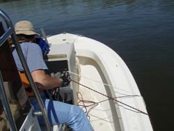 Person on a boat operating equipment with cables over the side in calm water.