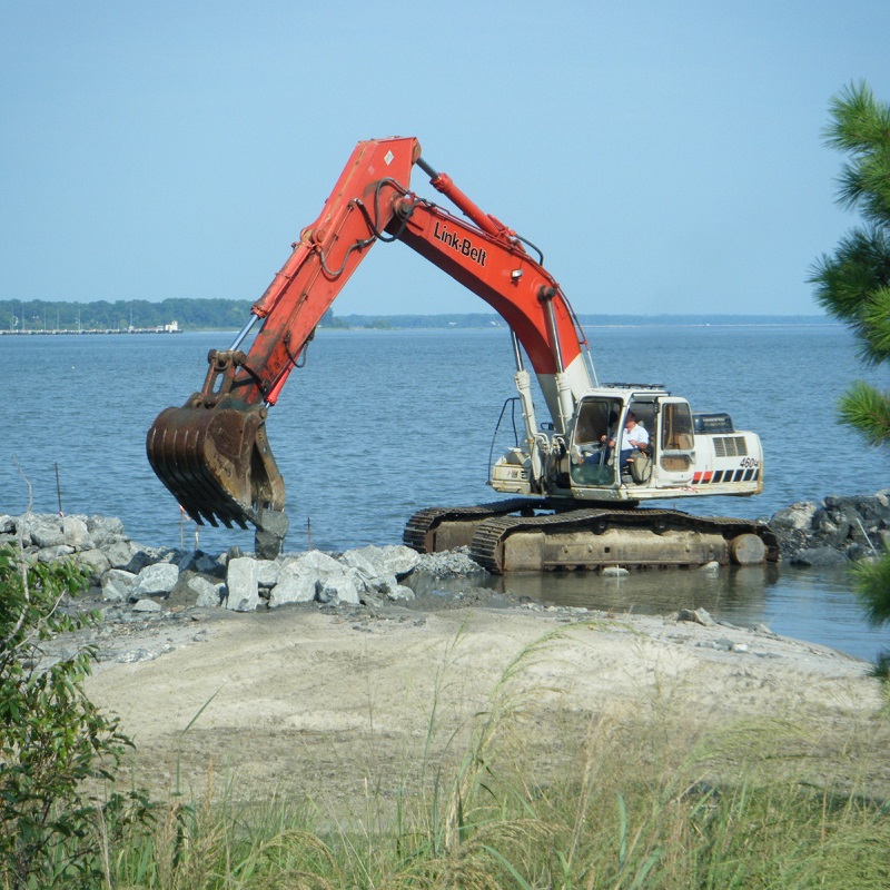 Excavator placing large rocks along a shoreline for erosion control construction